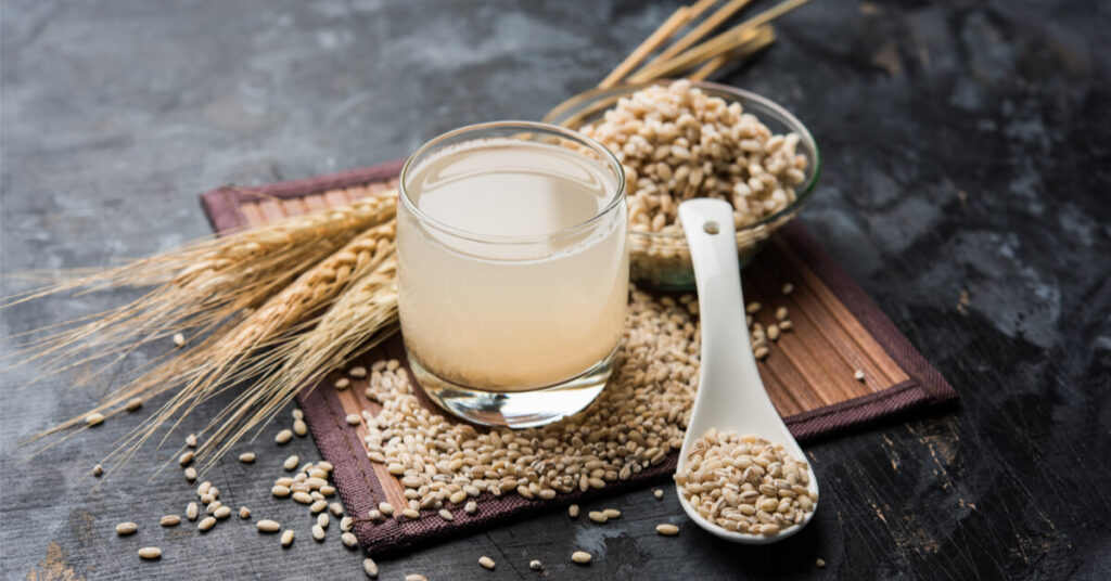 كوب شراب شعير طبيعي بجانب حبوب الشعير على طاولة خشبية يوضح فوائد شراب الشعير للكلى والهضم والجسم